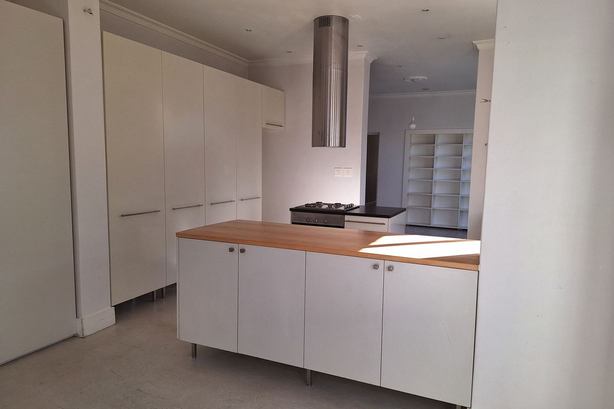 A modern, minimalist kitchen featuring white cabinetry, a central island with a wooden countertop, and a stainless steel extractor fan.