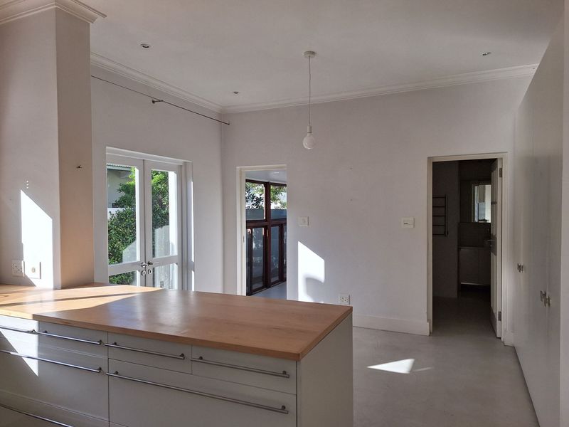 A bright, modern kitchen area featuring a central island with a wooden countertop, clean white cabinetry, and direct access to outdoor spaces.