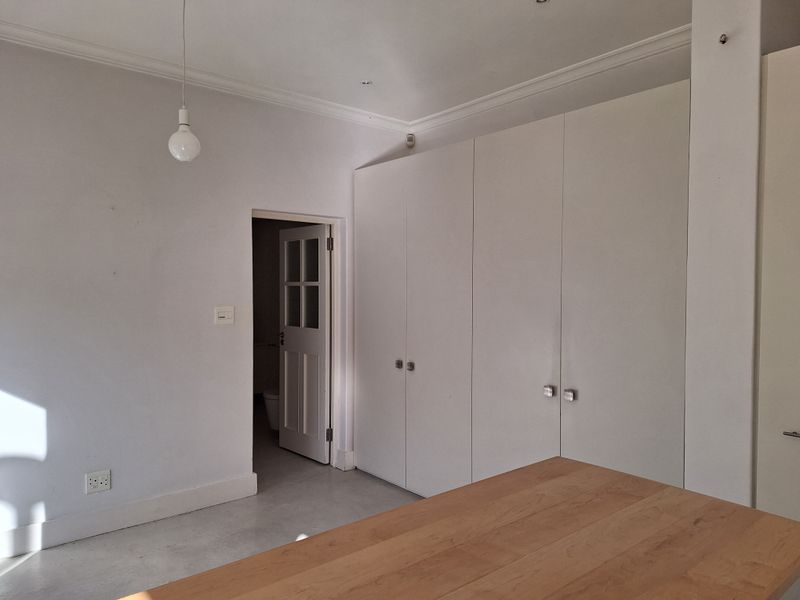 A bright, empty bedroom featuring neutral walls, tiled flooring, and ample built-in cupboard storage with a connecting door to an adjacent room.