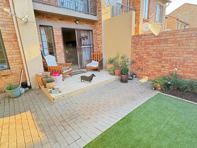 A private rear courtyard featuring a paved patio area, brick boundary walls, and a small section of artificial lawn, accessible via a sliding glass door.