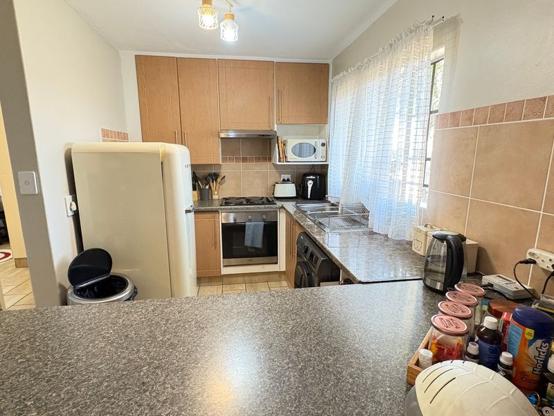 A functional kitchen featuring wood-finish cabinetry, laminate countertops, a built-in oven with gas hob, and a tiled backsplash.