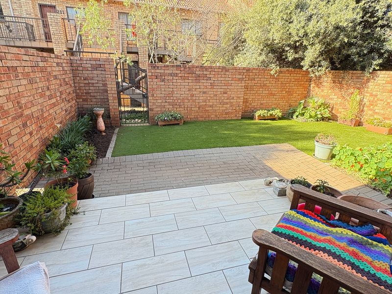 A private rear courtyard featuring a tiled patio area, artificial grass lawn, and secure brick boundary walls.