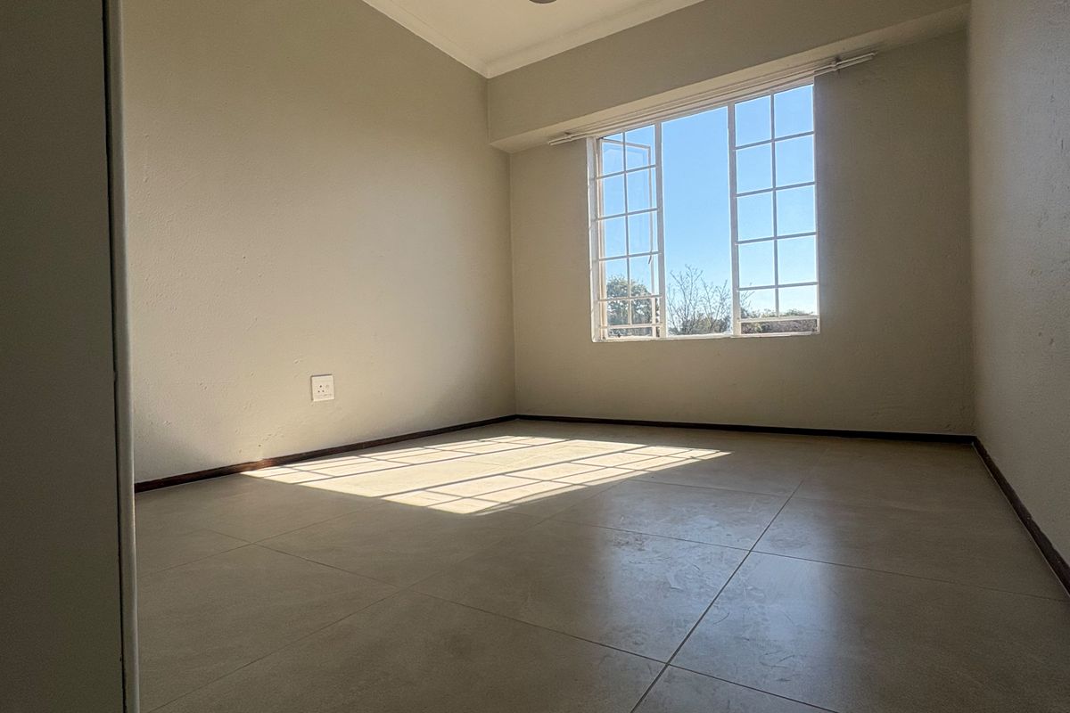 A bright, empty bedroom featuring neutral tiled flooring, a multi-pane window, and a modern pendant light fixture.
