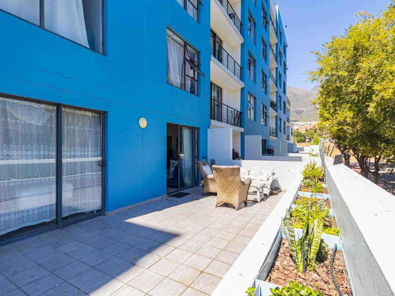 A spacious apartment balcony featuring tiled flooring, built-in planter boxes, and sliding glass door access to the interior living space.