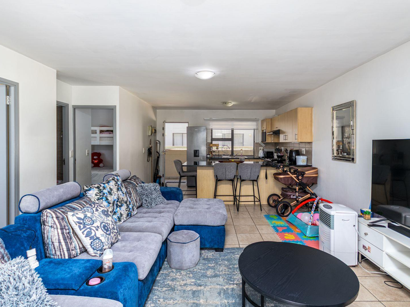 An open-plan living and kitchen area featuring tiled flooring, a functional kitchen island with breakfast bar seating, and direct access to an outdoor balcony.