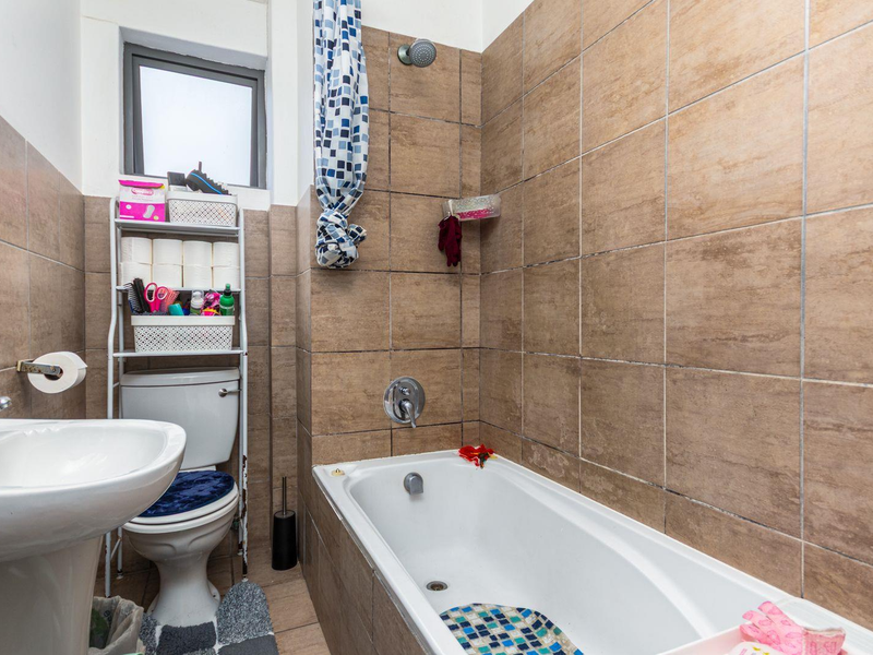 A functional bathroom featuring a pedestal washbasin, toilet, and a bathtub with shower mixer, finished with neutral wall and floor tiles.