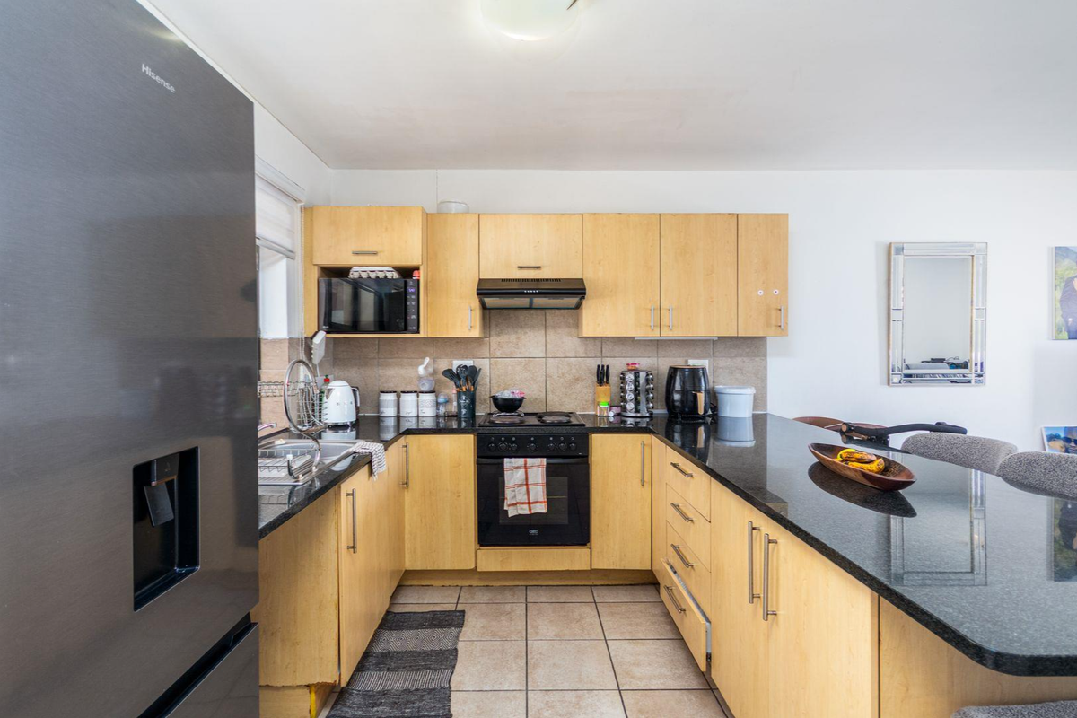 A functional kitchen featuring light wood cabinetry, black granite countertops, a built-in oven with hob, and a tiled backsplash.