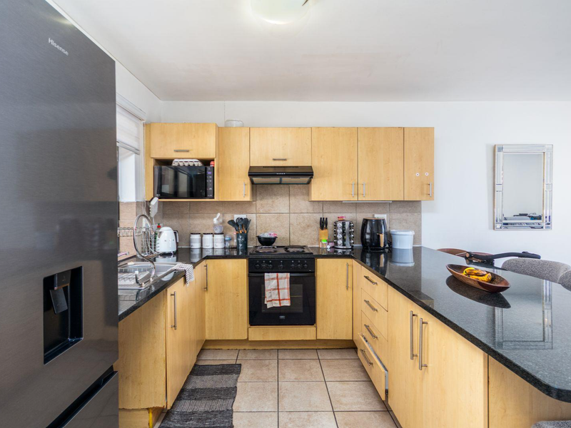 A functional kitchen featuring light wood cabinetry, black granite countertops, a built-in oven with hob, and a tiled backsplash.