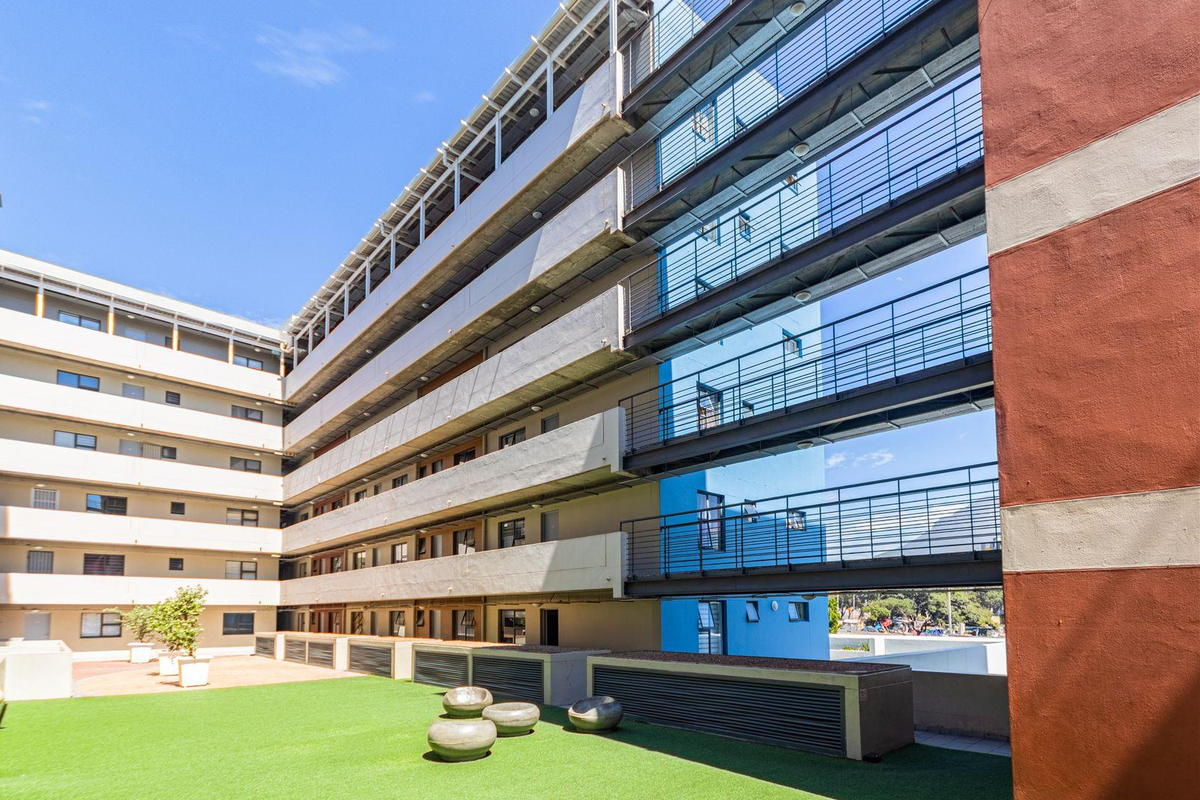 A view of the apartment complex exterior featuring multi-level metal walkways, concrete facade elements, and a landscaped courtyard area with artificial turf.