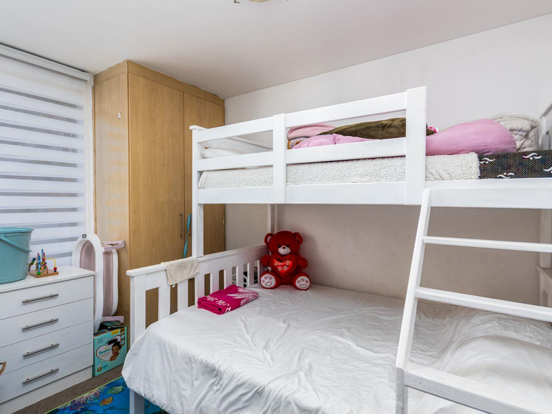 A functional bedroom featuring a built-in wardrobe and a window fitted with a modern roller blind.