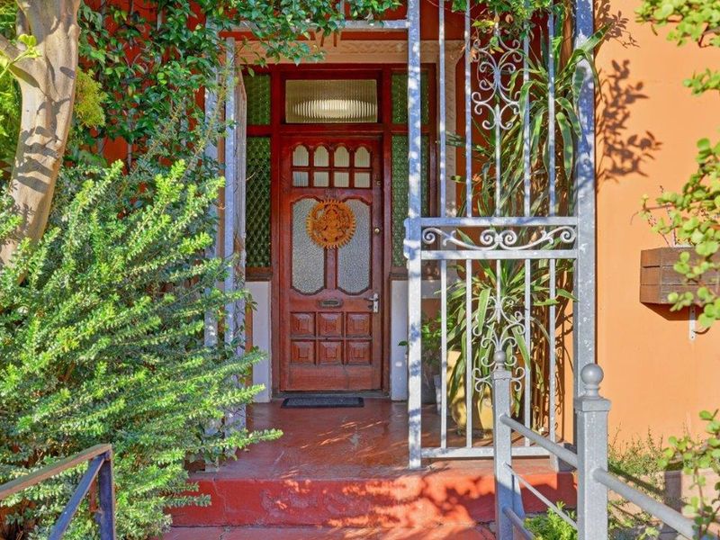 A charming entrance featuring a classic timber front door with transom window, protected by a decorative security gate and set on a tiled porch.