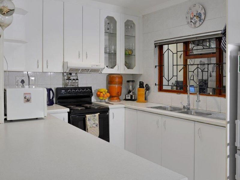 A functional kitchen featuring white cabinetry, laminate countertops, a double basin sink, and a tiled backsplash with a window overlooking the exterior.