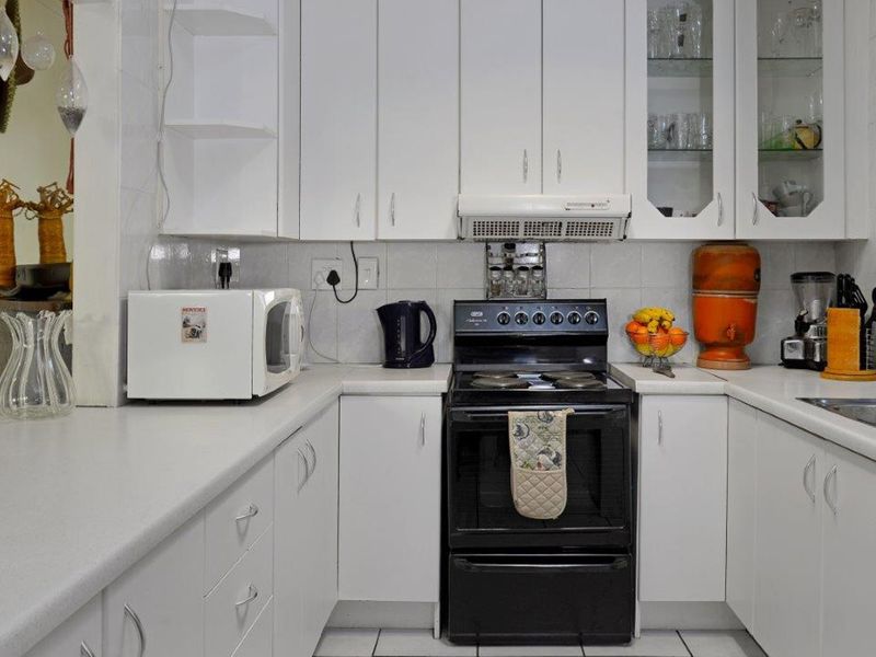 A functional kitchen featuring white cabinetry, laminate countertops, a tiled backsplash, and a freestanding oven with an integrated extractor fan.