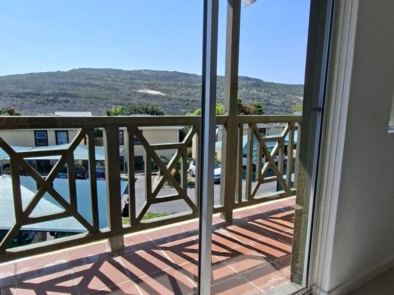 A balcony featuring tiled flooring and a wooden balustrade, offering an elevated view of the surrounding complex and landscape.