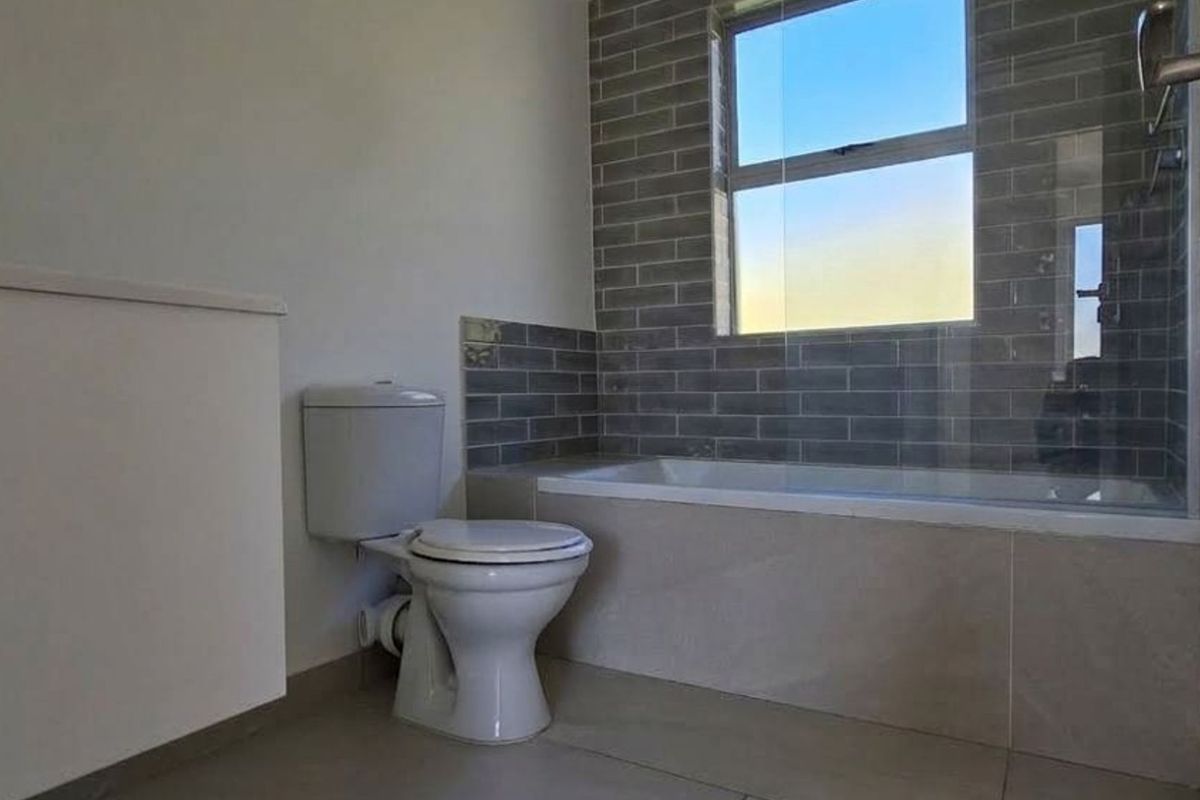 A clean, modern bathroom featuring a bathtub with a glass screen, subway tile surround, and a standard toilet.