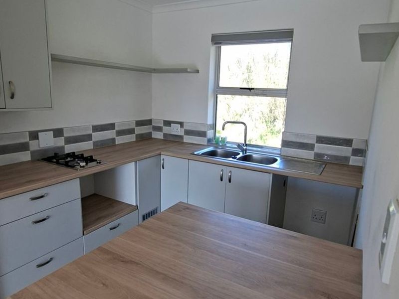 A clean, modern kitchen featuring light grey cabinetry, wood-look laminate countertops, a stainless steel double sink, and a built-in gas hob.