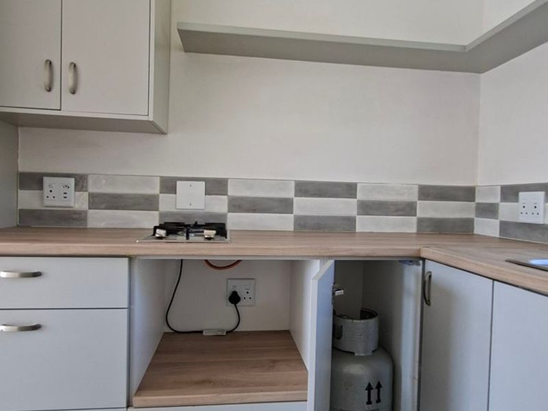 A clean, modern kitchen area featuring light-toned cabinetry, a wood-look laminate countertop, a gas hob, and a stylish grey and white tiled backsplash.