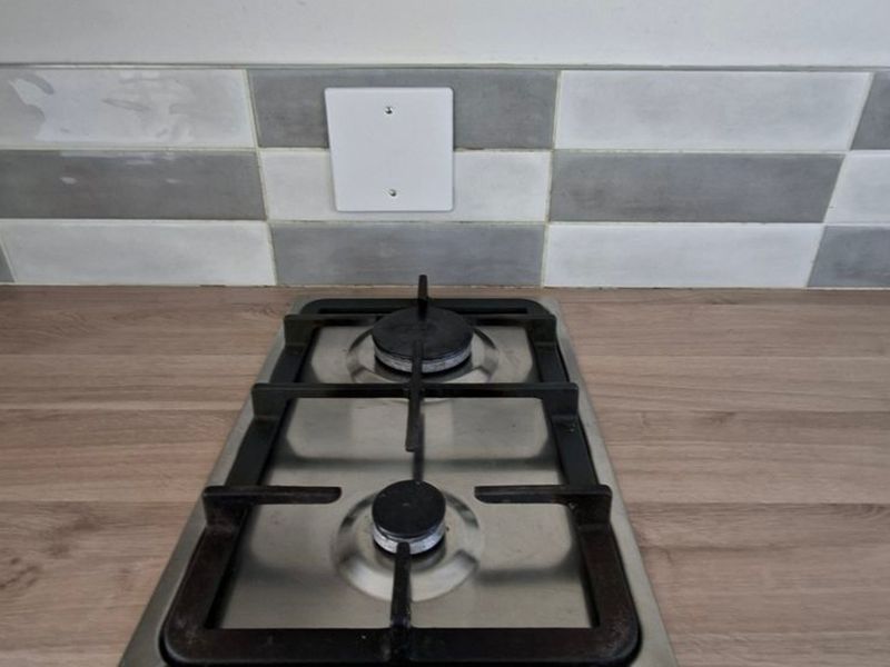 Close-up view of a two-burner gas hob set into a wood-look laminate countertop with a modern grey and white tiled backsplash.