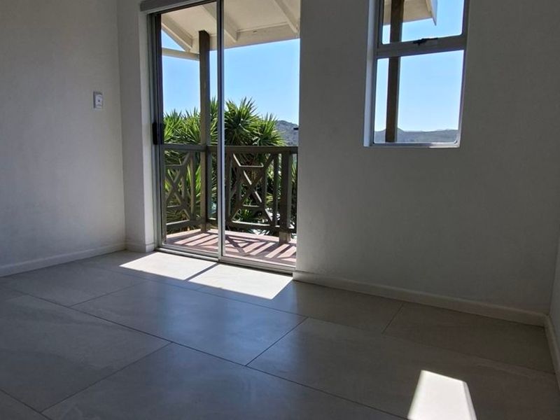 A bright, empty bedroom featuring neutral tiled flooring and a sliding glass door providing direct access to a private balcony with scenic views.