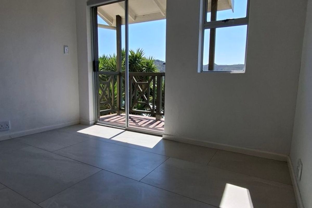 A bright, empty bedroom featuring neutral tiled flooring and a sliding glass door providing direct access to a private balcony with scenic views.