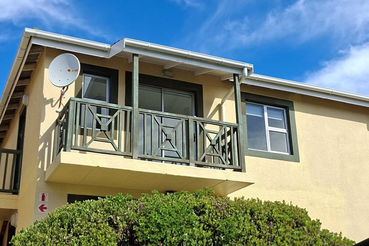 Exterior view of an apartment balcony featuring a timber balustrade, sliding glass door access, and a satellite dish installation.
