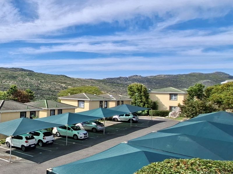 An elevated view of the apartment complex parking area featuring multiple shade cloth carports and well-maintained building exteriors set against a mountain backdrop.