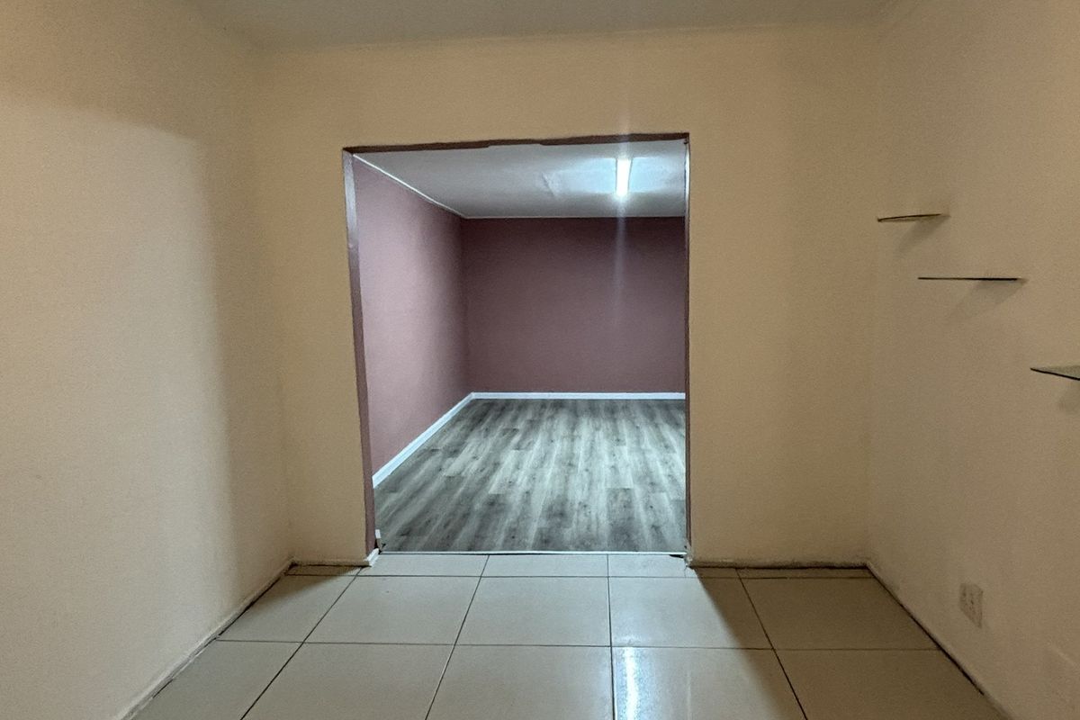 An empty living area featuring a combination of ceramic tiled and laminate flooring, with an open transition to an adjoining room.