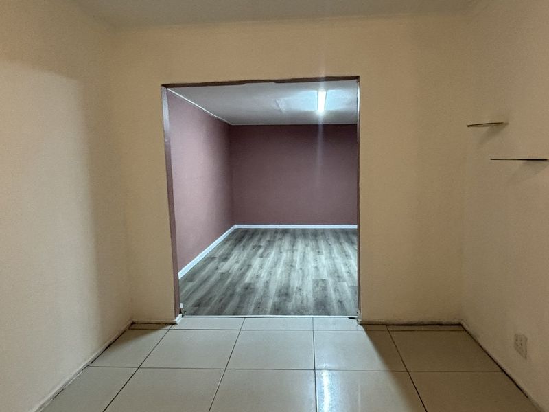 An empty living area featuring a combination of ceramic tiled and laminate flooring, with an open transition to an adjoining room.