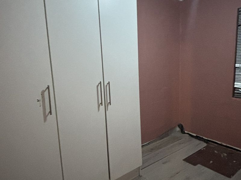 An empty bedroom featuring built-in cupboards, venetian blinds, and laminate flooring in need of repair.