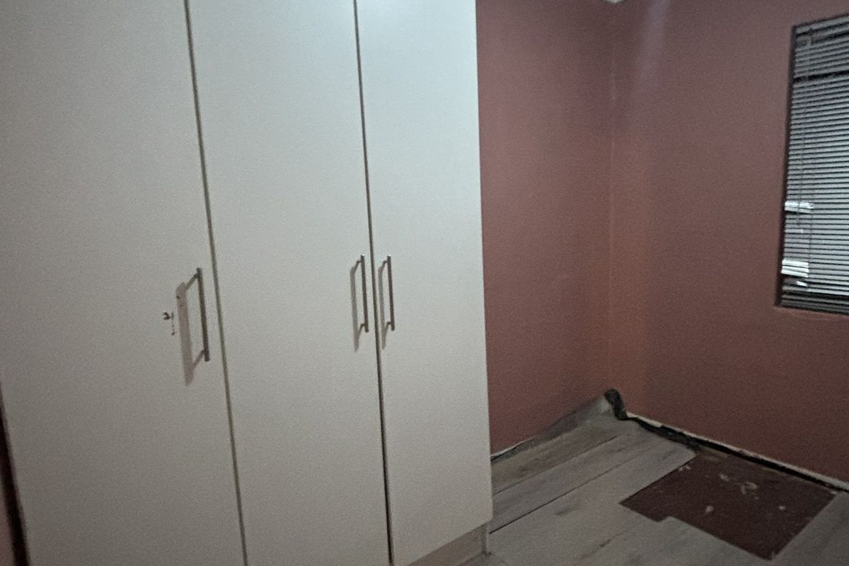 An empty bedroom featuring built-in cupboards, venetian blinds, and laminate flooring in need of repair.