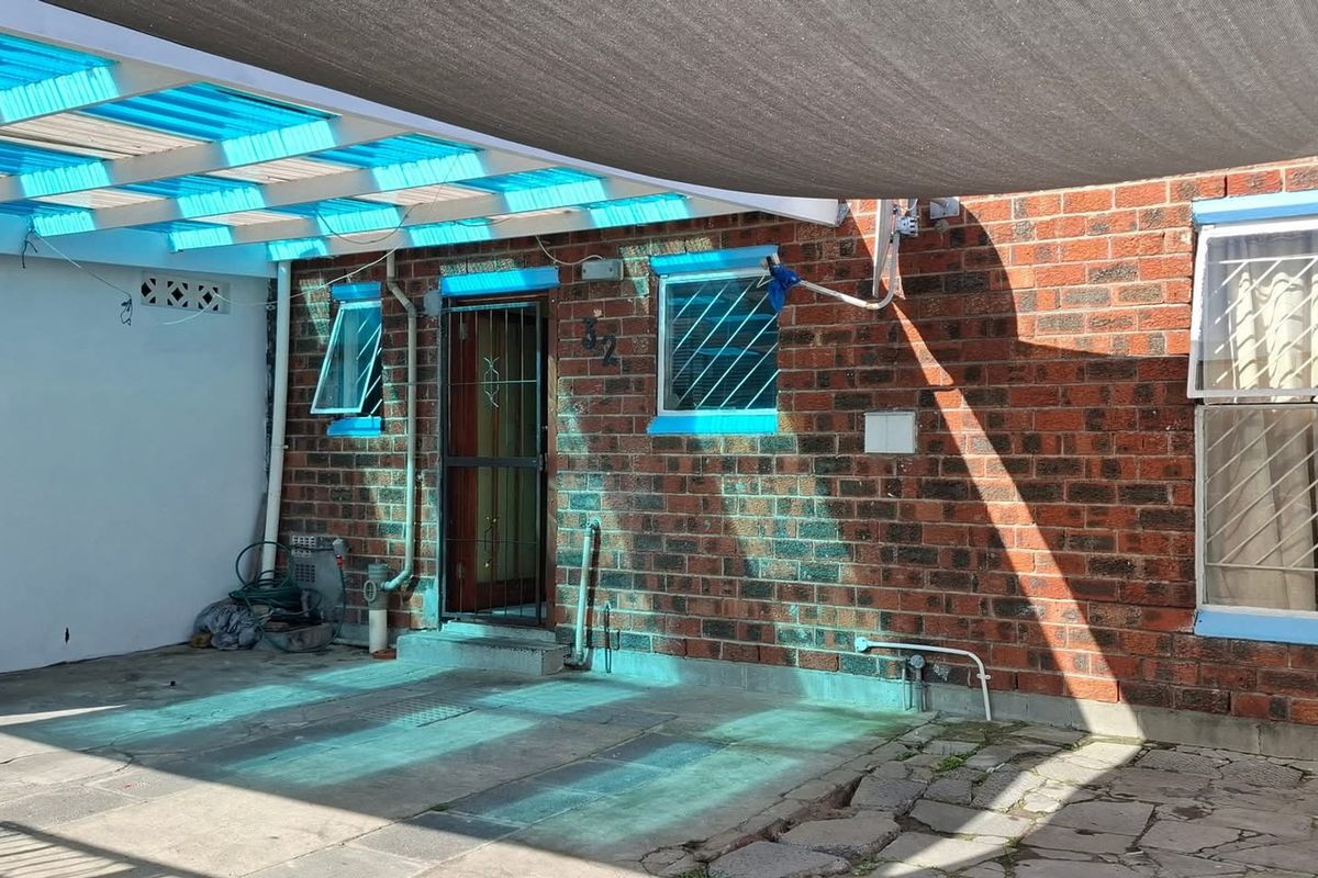 Rear exterior area featuring a brick facade, paved patio, and a covered outdoor space with a shade sail and polycarbonate roofing.