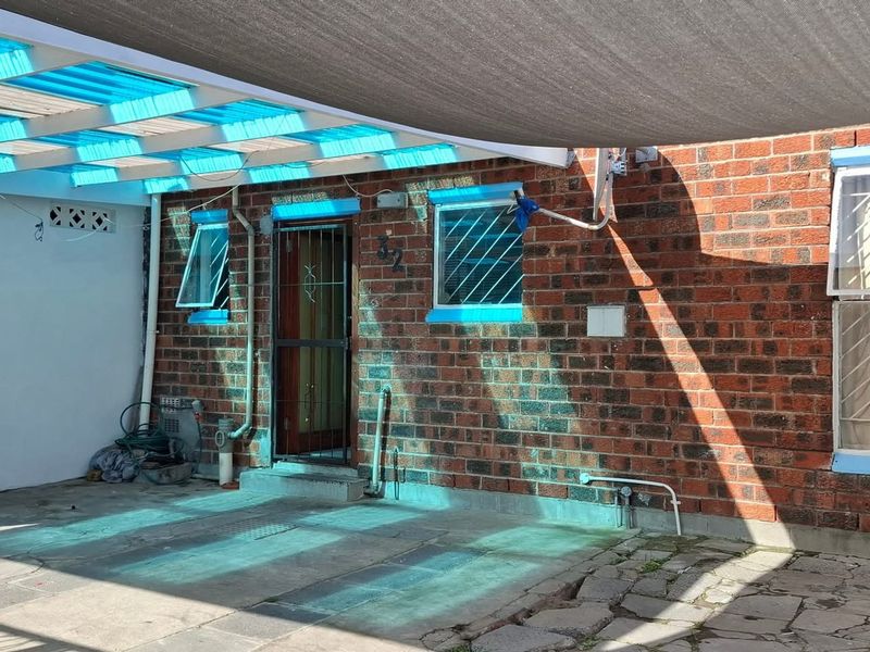 Rear exterior area featuring a brick facade, paved patio, and a covered outdoor space with a shade sail and polycarbonate roofing.
