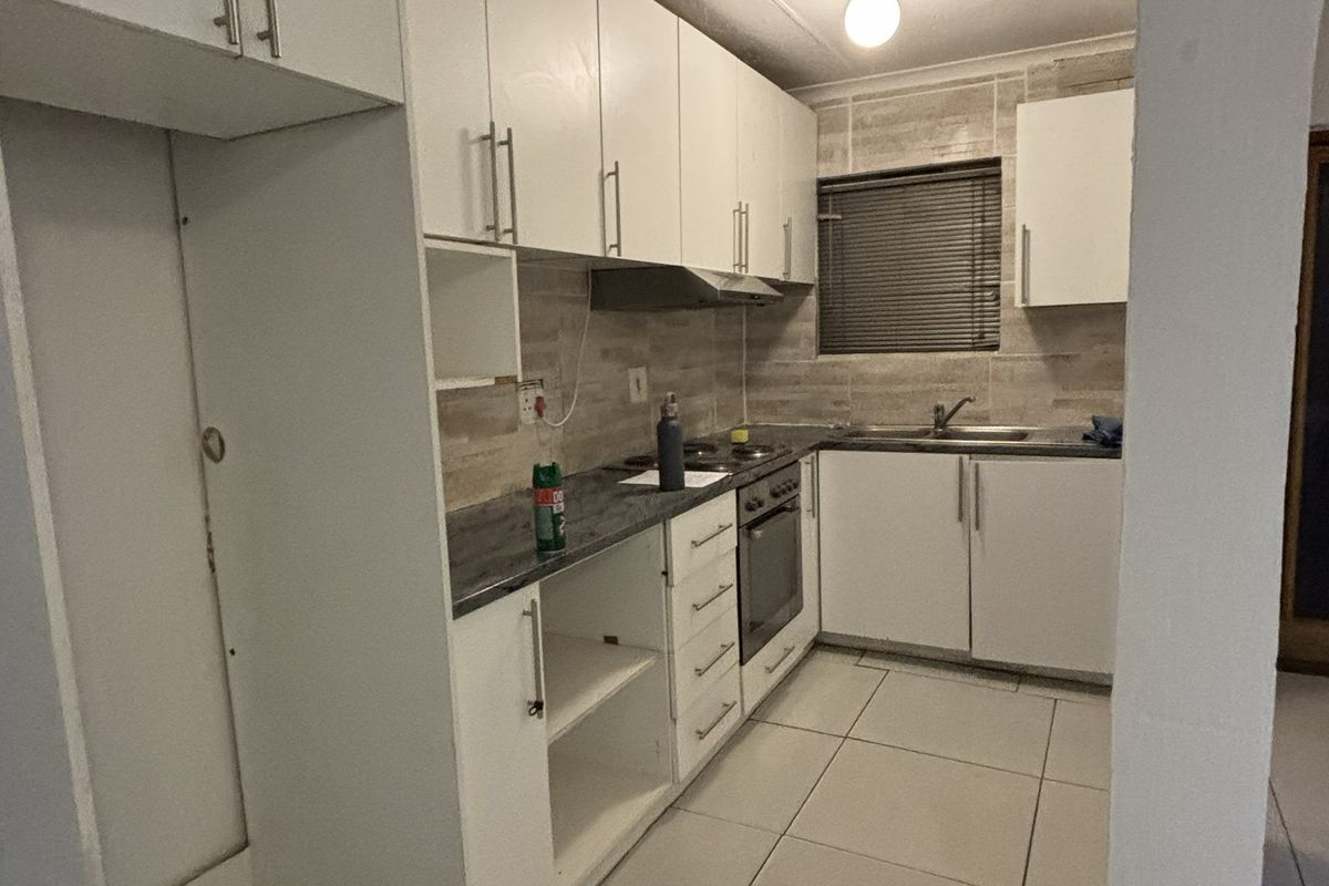 A functional kitchen featuring white cabinetry, laminate countertops, a built-in oven, extractor fan, and tiled backsplash with neutral floor tiles.