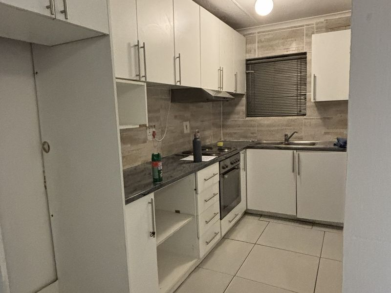 A functional kitchen featuring white cabinetry, laminate countertops, a built-in oven, extractor fan, and tiled backsplash with neutral floor tiles.