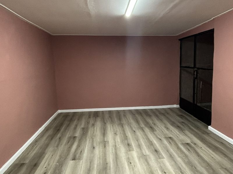 A clean, empty bedroom featuring modern laminate flooring, neutral pink walls, and a glass panel door, providing a versatile space ready for personalization.