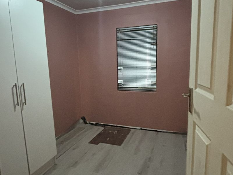 An empty bedroom featuring laminate flooring, a built-in wardrobe, and venetian blinds, currently requiring minor finishing work to the flooring and baseboards.