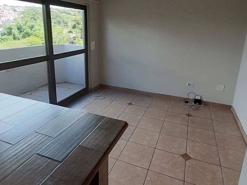 An empty living area featuring tiled flooring, a built-in counter, and a sliding glass door providing access to an outdoor balcony.