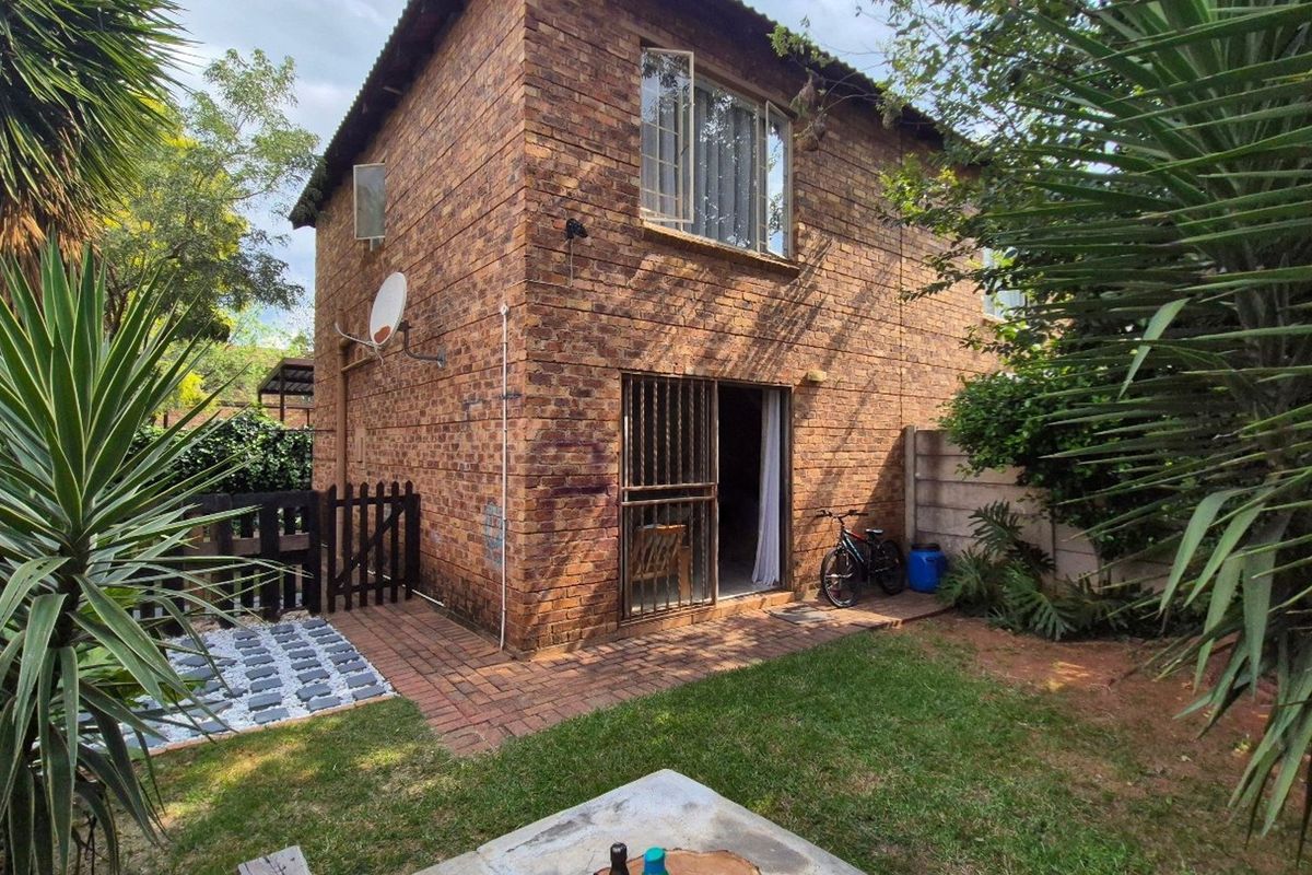 Rear view of a face brick apartment building featuring a paved patio area, small garden, and secure sliding door access.