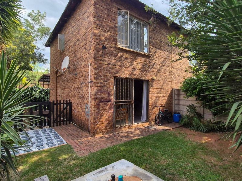 Rear view of a face brick apartment building featuring a paved patio area, small garden, and secure sliding door access.