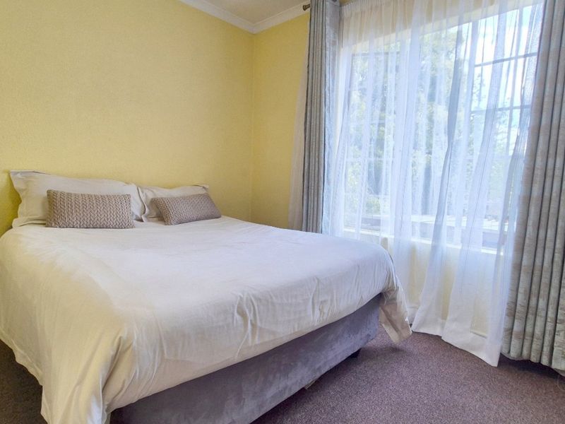 A standard bedroom featuring carpeted flooring and a large window with installed curtain tracks, providing natural light to the space.