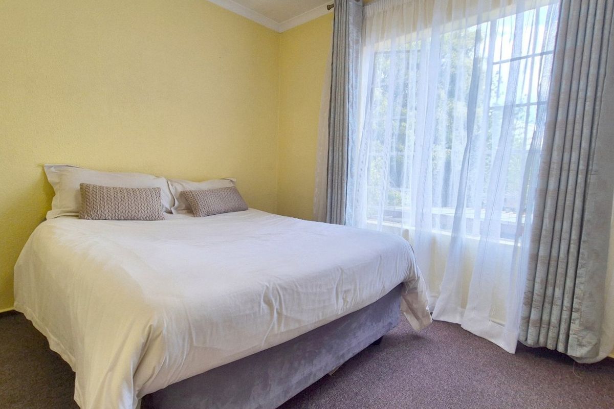 A standard bedroom featuring carpeted flooring and a large window with installed curtain tracks, providing natural light to the space.
