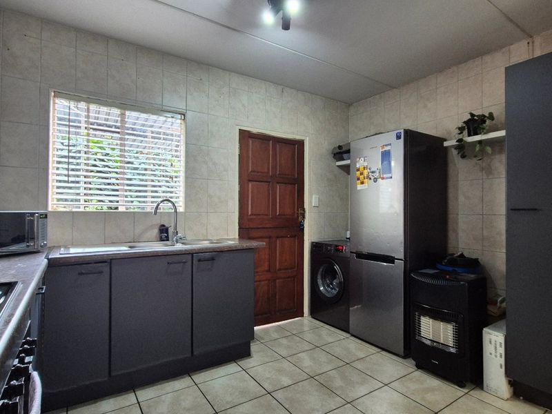 A functional kitchen featuring dark cabinetry, tiled backsplash, laminate countertops, and integrated appliances, providing a practical workspace with direct access to an exterior door.
