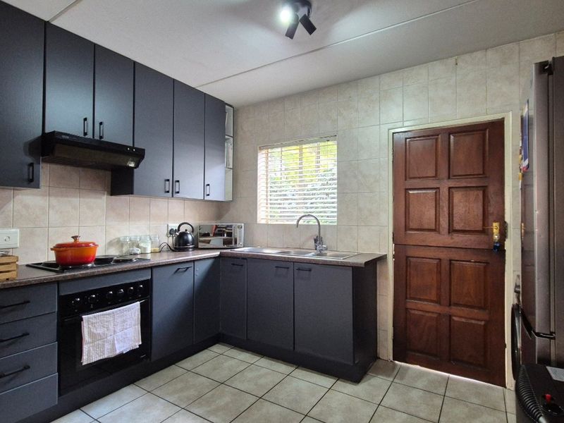 A functional kitchen featuring dark grey cabinetry, laminate countertops, built-in oven and hob, tiled backsplash, and tiled flooring with a rear access door.