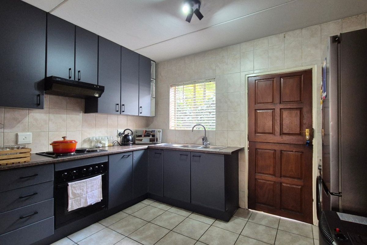 A functional kitchen featuring dark grey cabinetry, laminate countertops, built-in oven and hob, tiled backsplash, and tiled flooring with a rear access door.