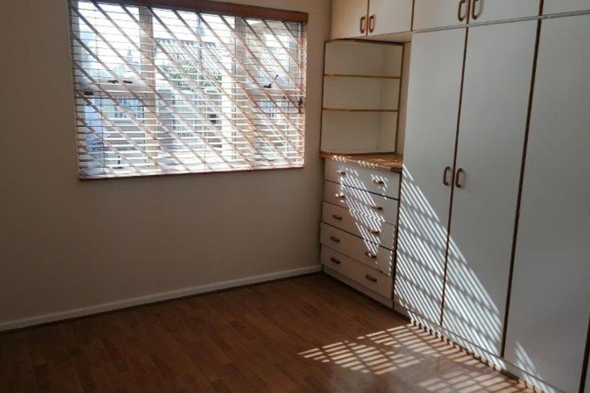 A bright, empty bedroom featuring laminate flooring and extensive built-in cupboard storage with integrated shelving and drawers.