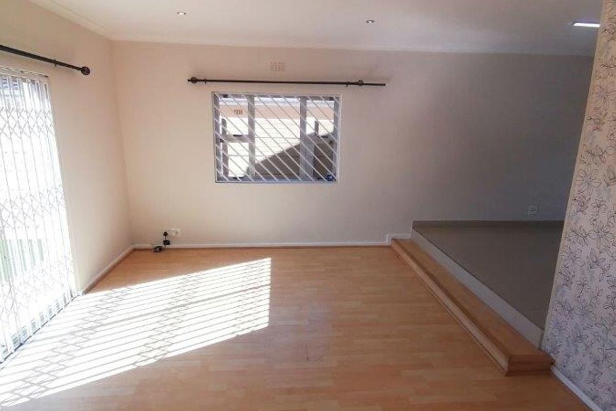 An empty living room featuring laminate flooring, a raised platform area, and security fixtures on the windows and sliding door.