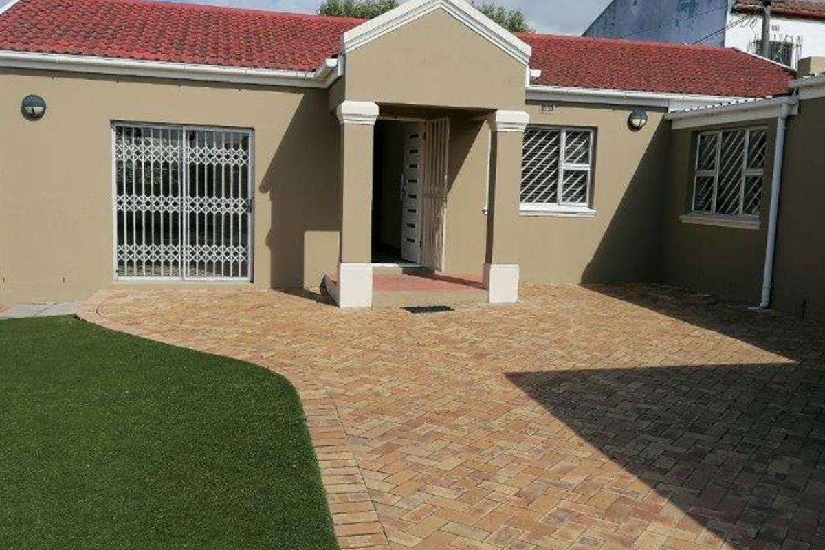 Rear exterior view of the house featuring a paved courtyard, artificial lawn, and secure access points with fitted security gates and bars.
