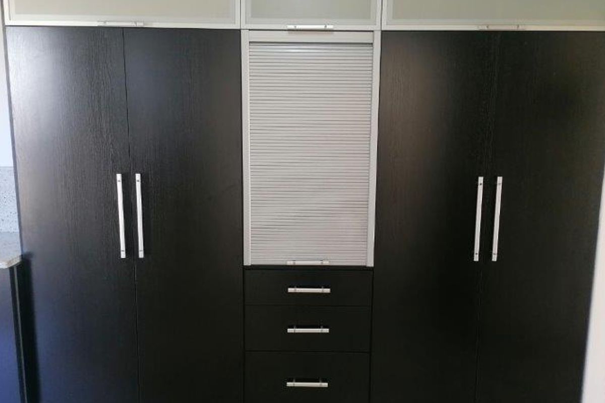 A modern kitchen featuring dark wood built-in cabinetry, integrated drawers, and a convenient roller shutter appliance garage for organized storage.