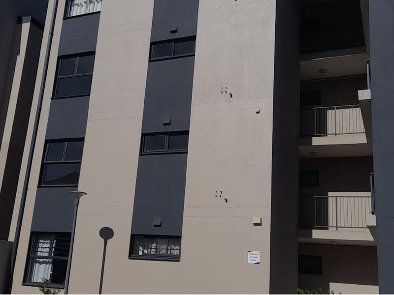 A modern multi-story apartment building facade featuring neutral tones, dark accent panels, and private balconies with metal railings.