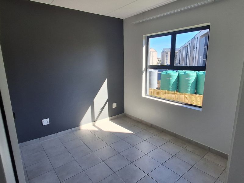 A bright, empty bedroom featuring neutral tiled flooring, a dark grey accent wall, and an aluminium-framed window with exterior views.